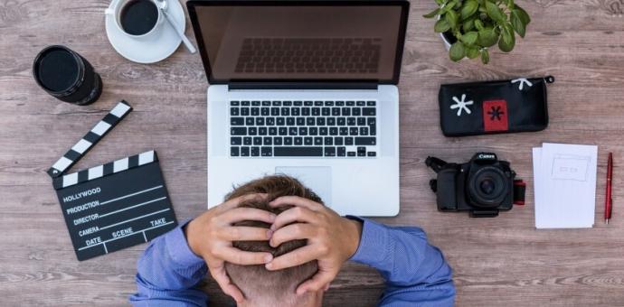 Foto de homem sentado na mesa com computador e mãos na cabeça