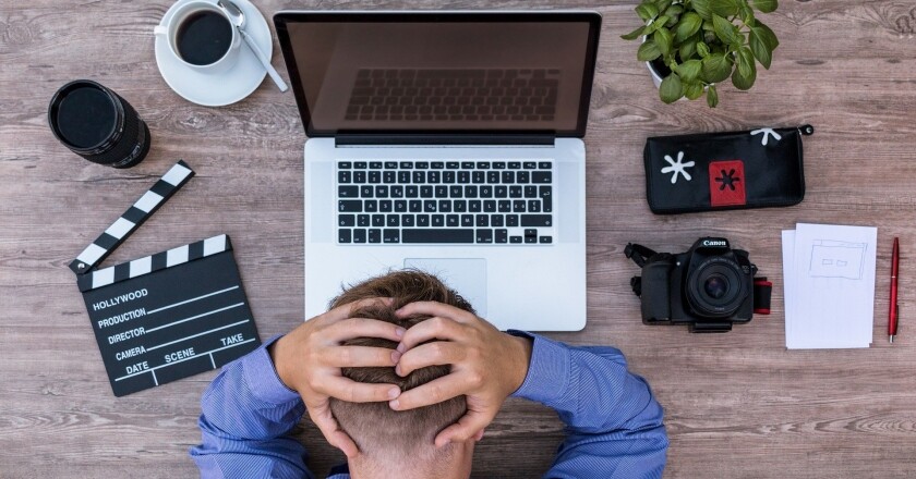 Foto de homem sentado na mesa com computador e mãos na cabeça