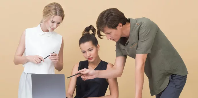 Foto de 3 pessoas olhando para um computador e analisando algo